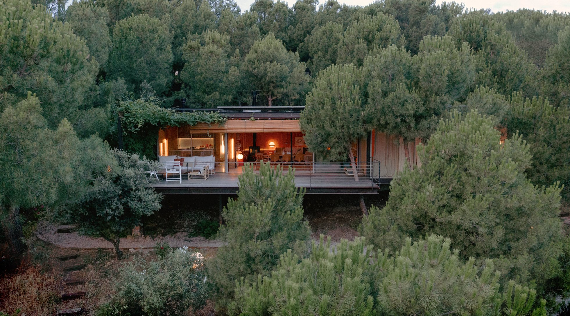 Casa modular Tini iluminada al anochecer entre pinos, con la terraza elevada sobre el bosque