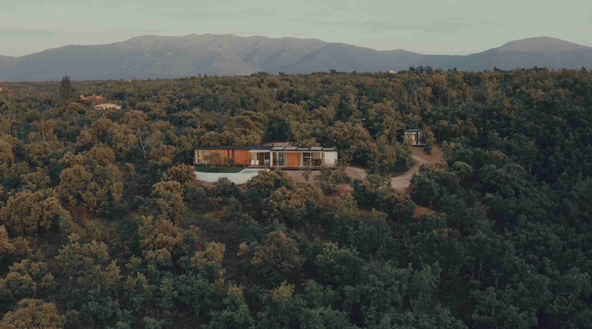 Vista aérea de una casa modular Tini Living con piscina rodeada de encinar y montañas al fondo