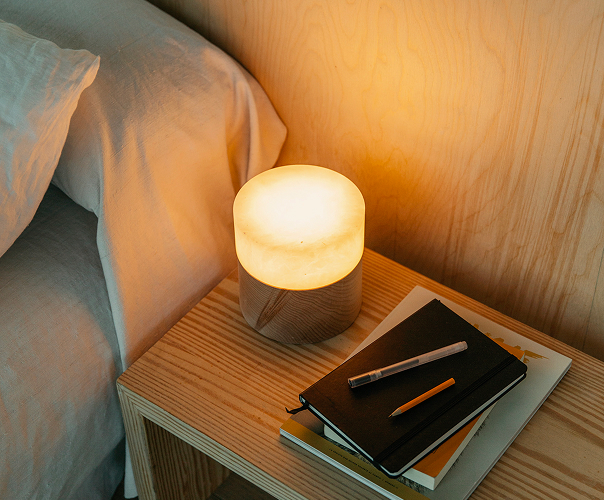 Detalle del dormitorio de la Tini M: mesilla de madera con lámpara cálida junto a la cama