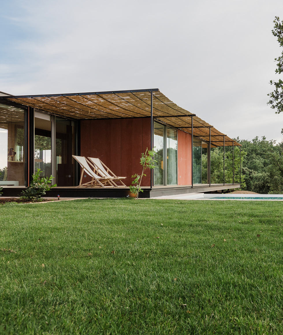 Porche de la casa modular Tini M con pérgola de cañizo, tumbonas y jardín con piscina